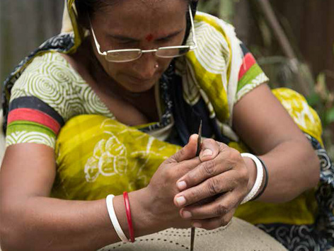 A woman wears glasses while decorating pottery.