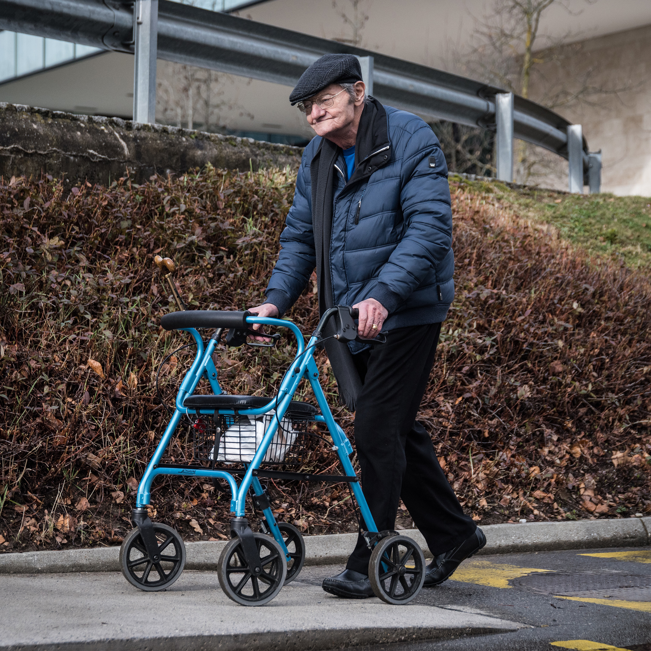 An older man using a rollator outdoors on a concrete path.