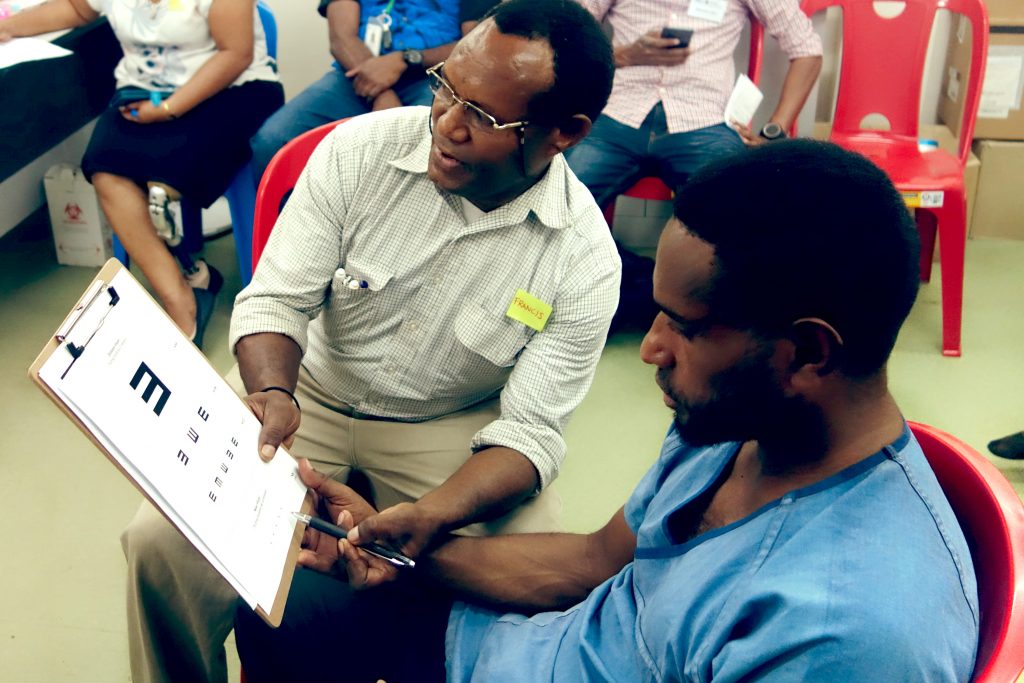 A service provider holds a clipboard showing an E-Chart in front of a client. They are gesturing to the small Es with a pen.