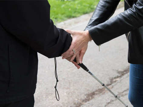 A person helping someone to hold onto a white cane.