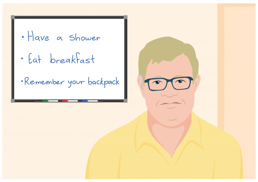 Samuel wears prescription glasses and stands in front of his whiteboard. His board reads: have a shower, eat breakfast, remember your backpack.