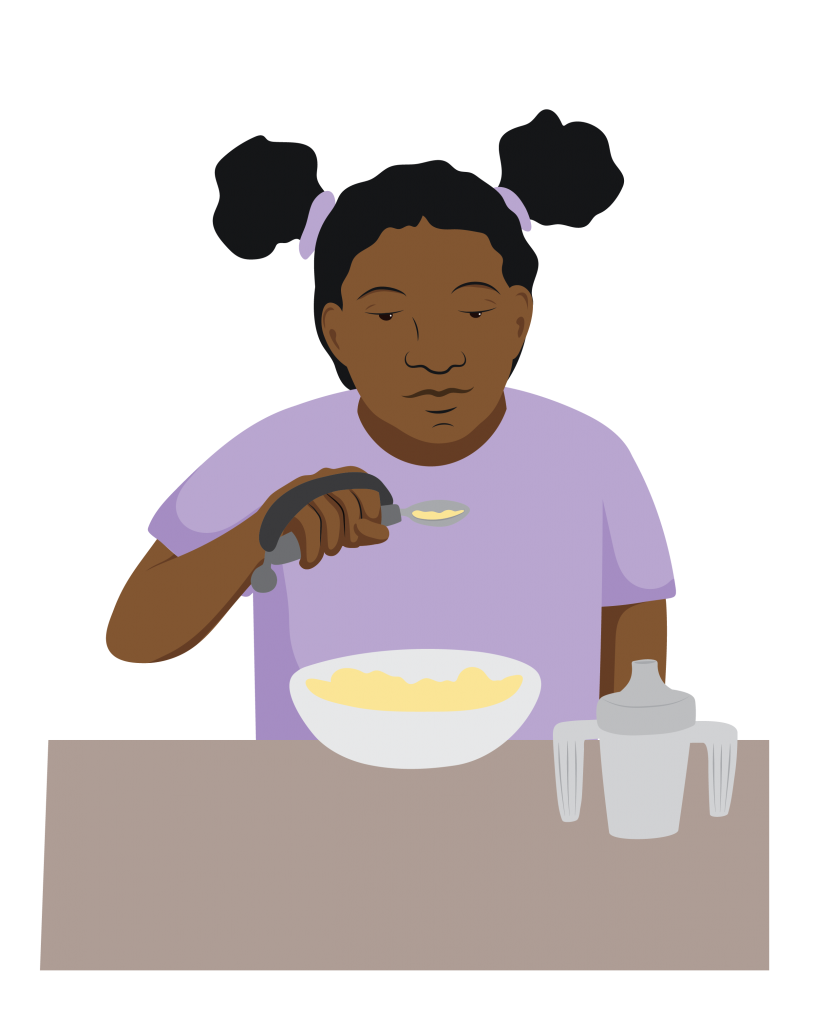 Aleisha at a table, holding a spoon with the help of a strap over her hand. She has picked up her food from a bowl which is next to a modified cup with two handles.