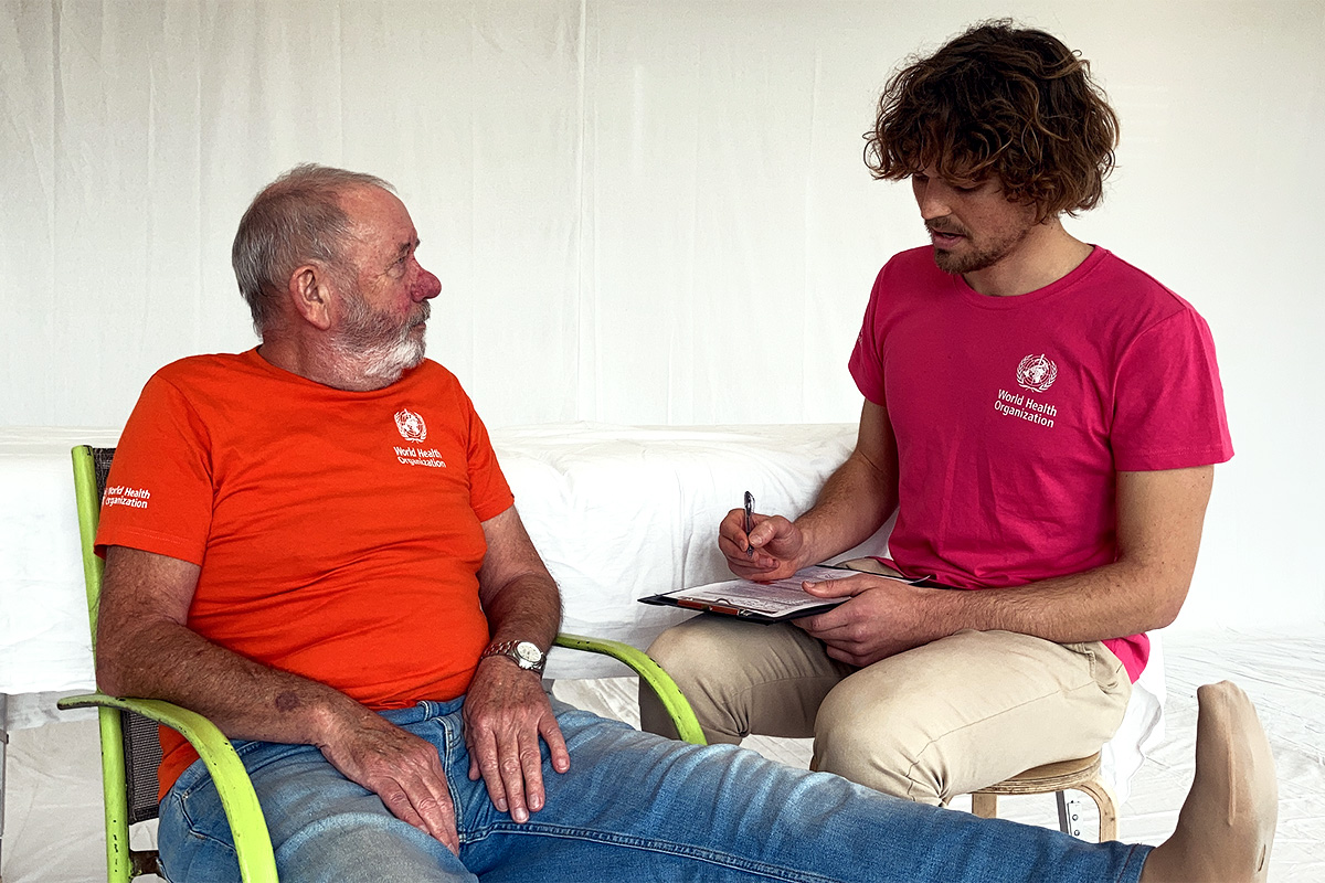 A man sitting in a chair with his foot propped up in front of him speaks to a service provider who is taking notes.
