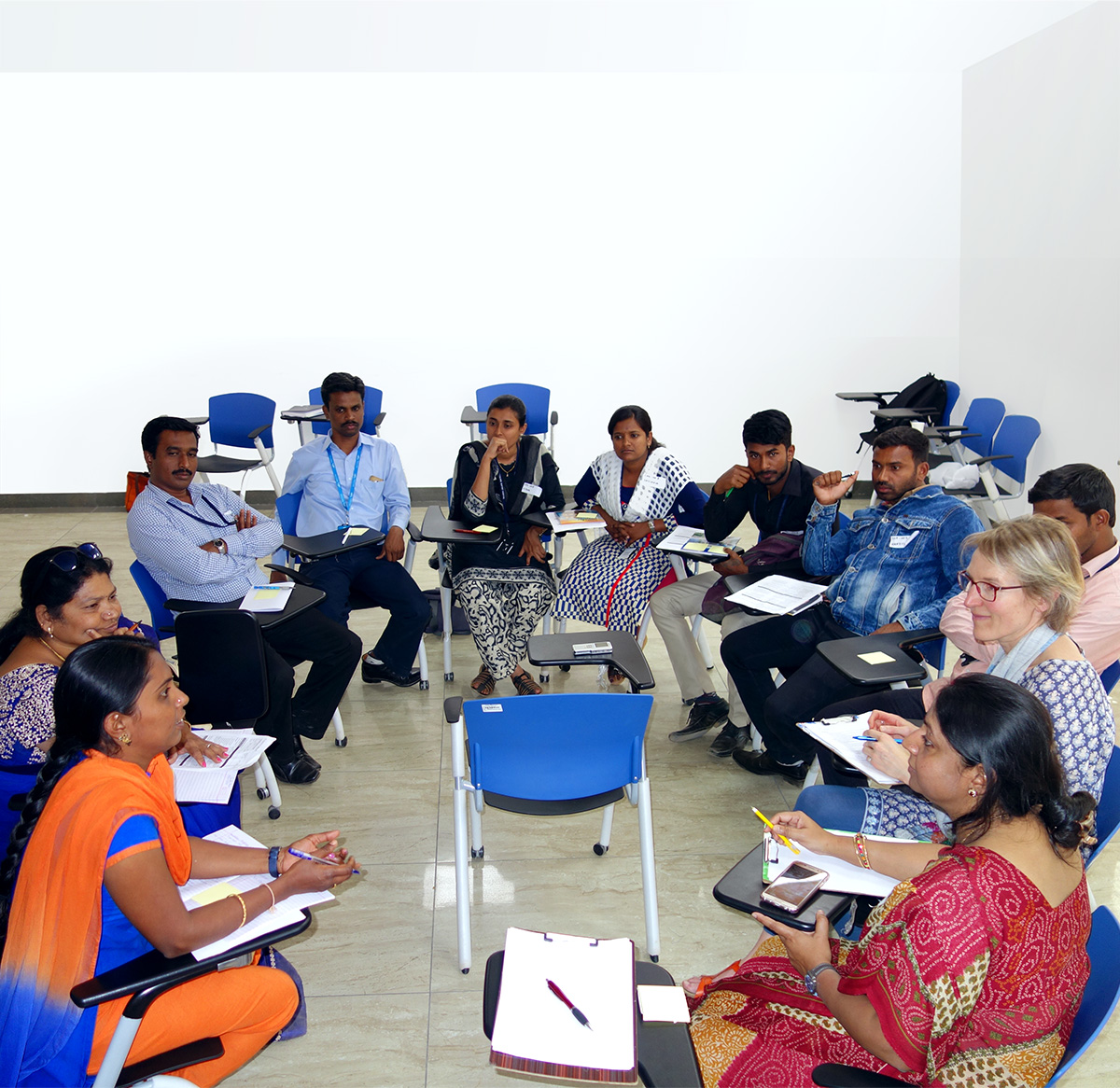 A group of 11 people sit in a circle. Some are holding notes and pens. A discussion is going on between a few, the others are listening carefully.