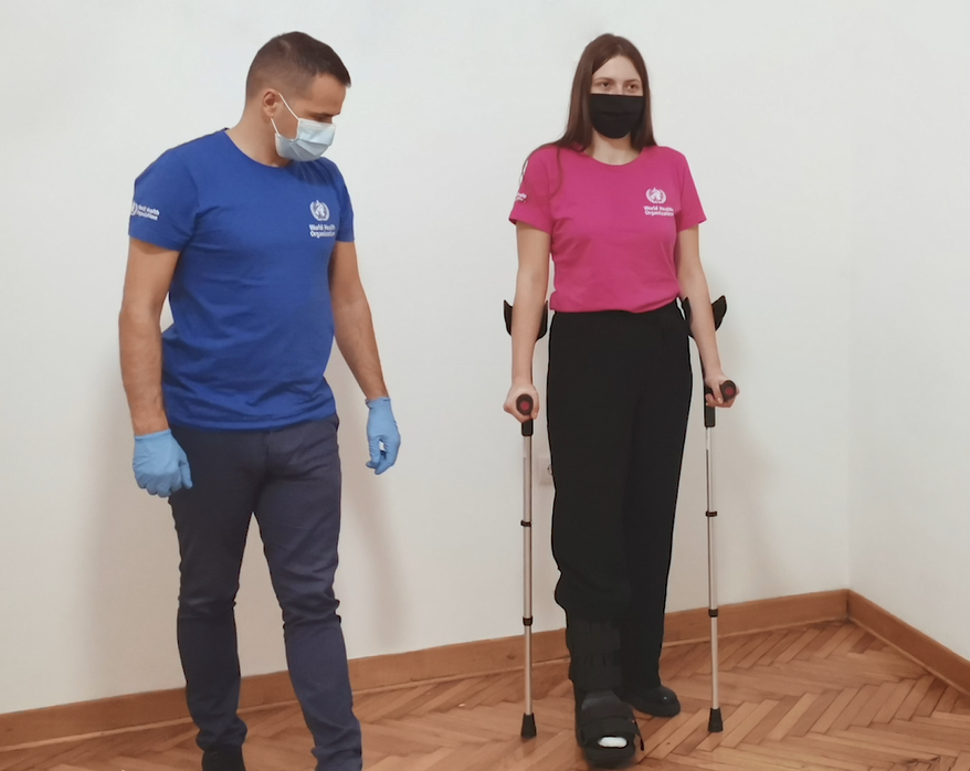 Person wearing rigid removable boot with crutches standing next to clinician