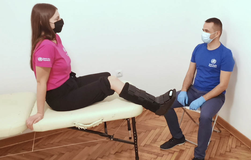 Person wearing rigid removable boot, sitting on treatment bed with clinician sitting in front of them