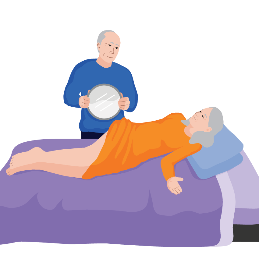 Verna lies on her side while her husband holds a mirror to help her check the skin on her buttocks for signs of pressure wounds.