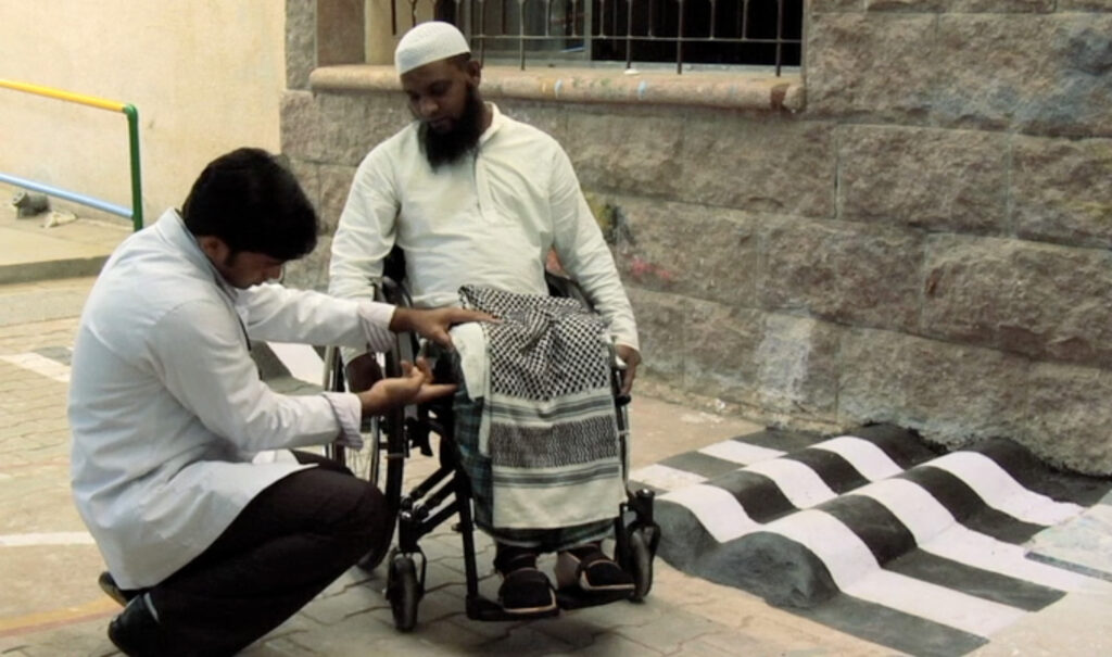 A man using a wheelchair and ankle supports has his leg position checked by a health worker.