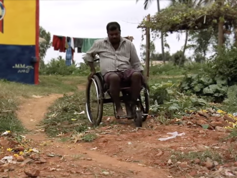 A man propels a wheelchair over rough uneven ground.