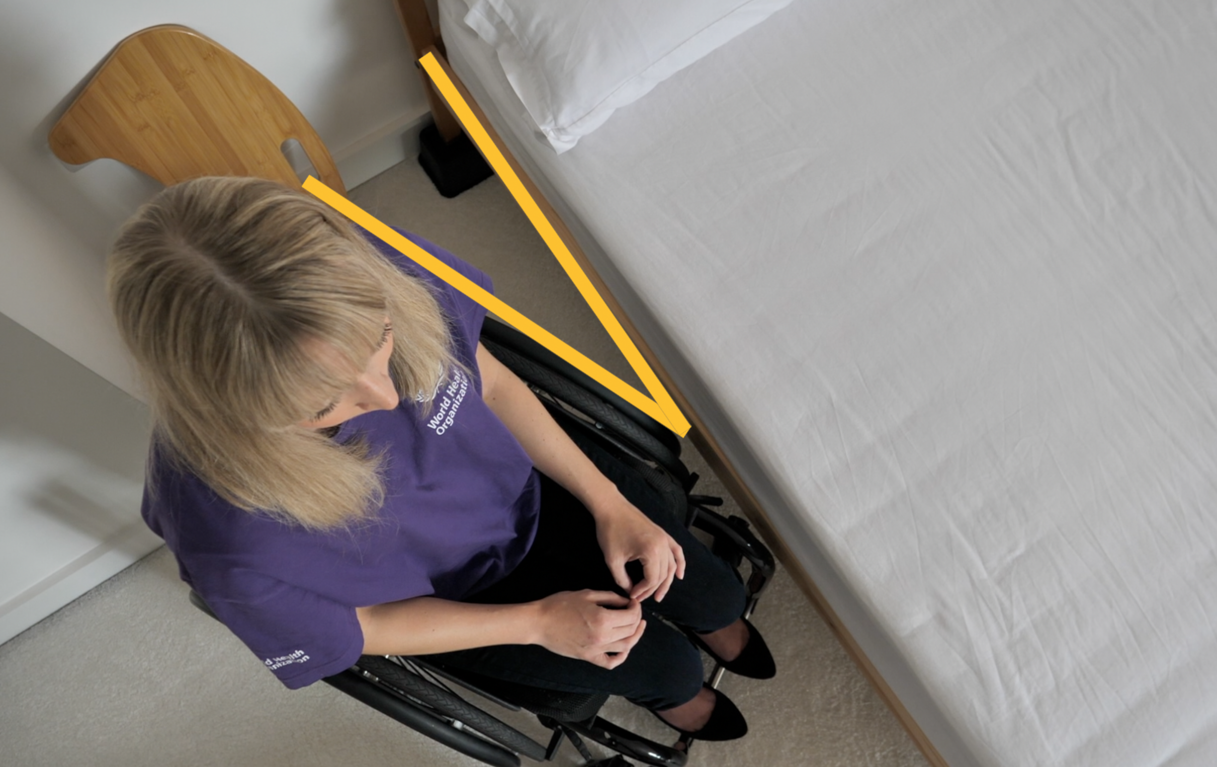 A person is positioning the wheelchair at an angle to the bed.