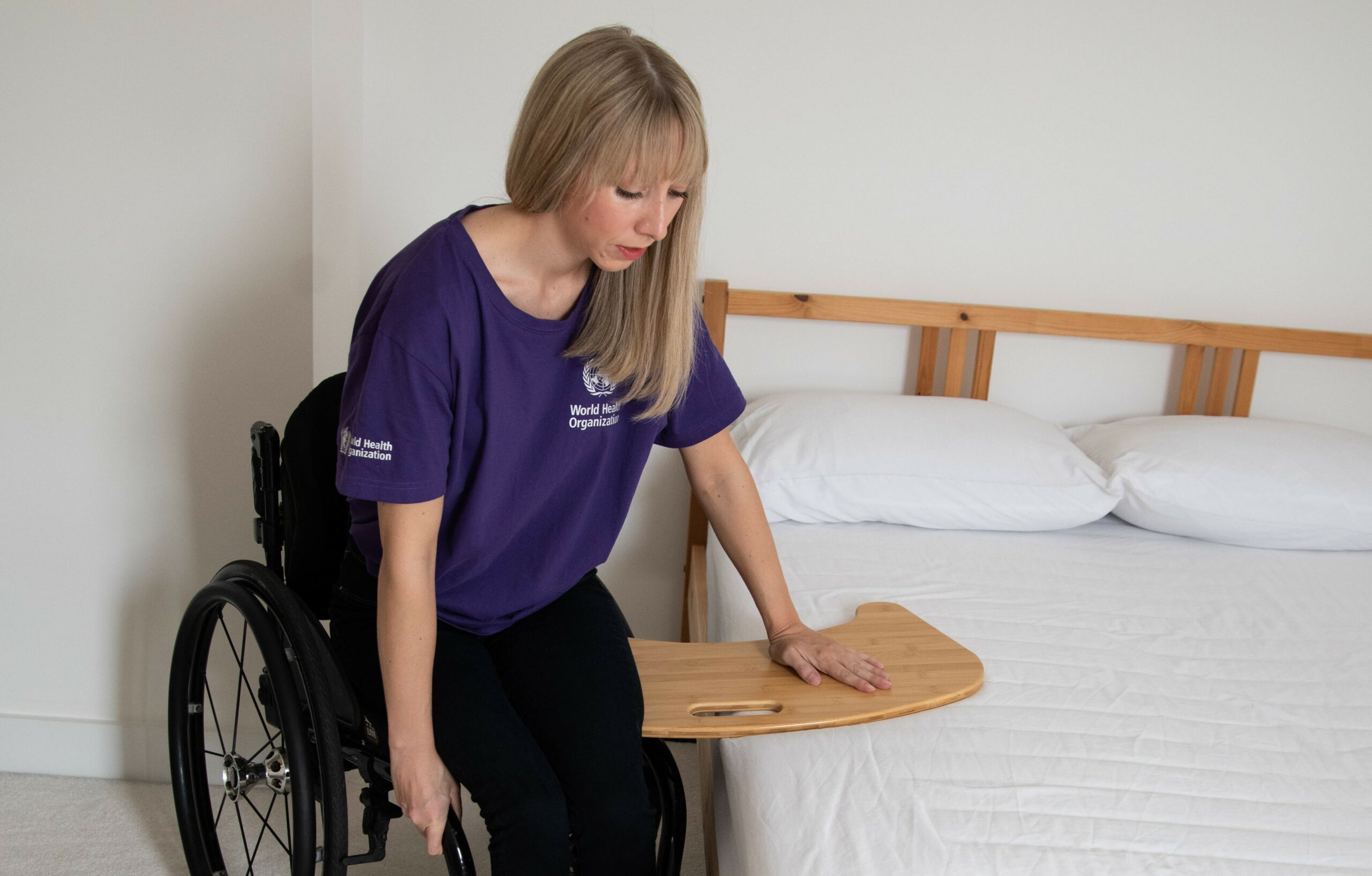A person pushes through their arms and shifts weight off their buttocks to lift across the transfer board.