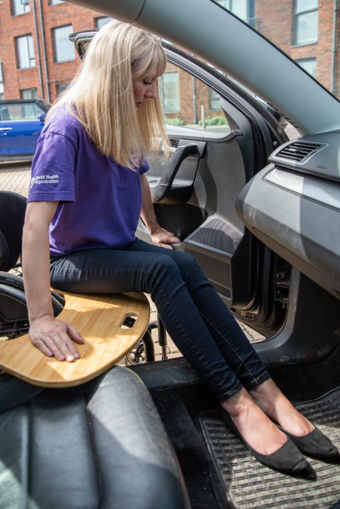 Front view of a person transferring from a wheelchair into a vehicle with their feet first, using a curved transfer board.
