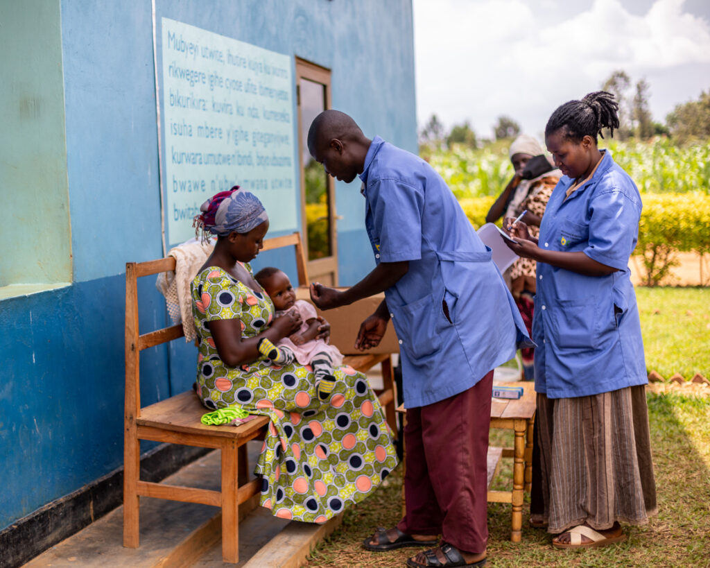 A baby being held by a person while a health worker drops Vitamin A supplement in the baby’s mouth.